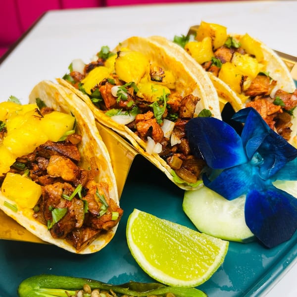 Three Magic Restaurant tacos with meat, pineapple, cilantro, and onions, garnished with lime and a blue orchid.