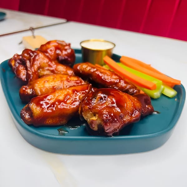 Magic Restaurant's Latin-American style chicken wings with sauce, celery, and carrots on a teal plate.