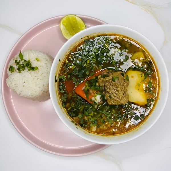 Hearty Latin-American beef soup with potatoes, vegetables, and cilantro, served with white rice and lime.