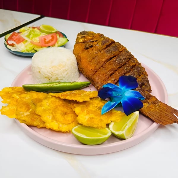 A Latin-American fried fish dish with rice, plantains, lime, and a blue orchid garnish.