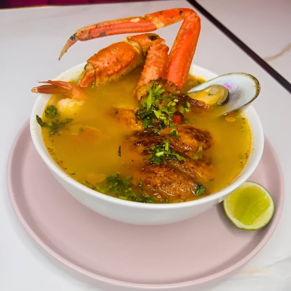 Latin-American seafood soup with crab legs, mussels, and fried fish, garnished with cilantro and lime.