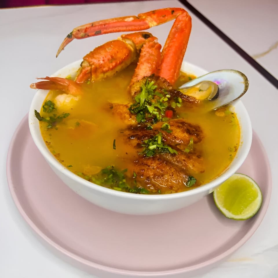 Latin-American seafood soup with crab legs, mussels, and fried fish, garnished with cilantro and lime.