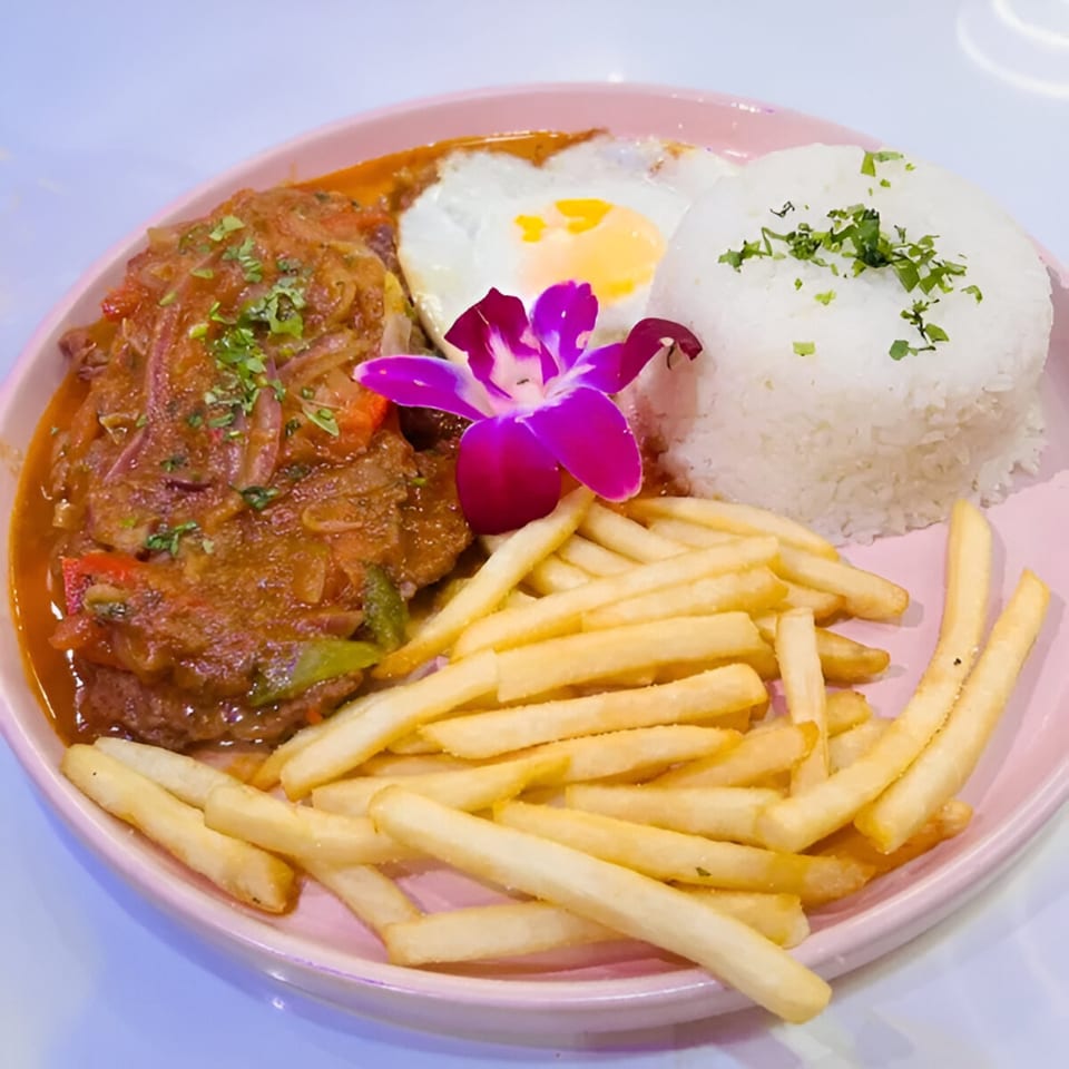 Latin-American dish with stewed meat, fried egg, white rice, french fries, and a purple orchid.
