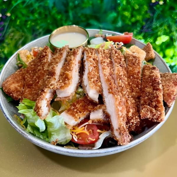 Crispy breaded chicken slices on a fresh salad with tomatoes, cheese, and dressing.